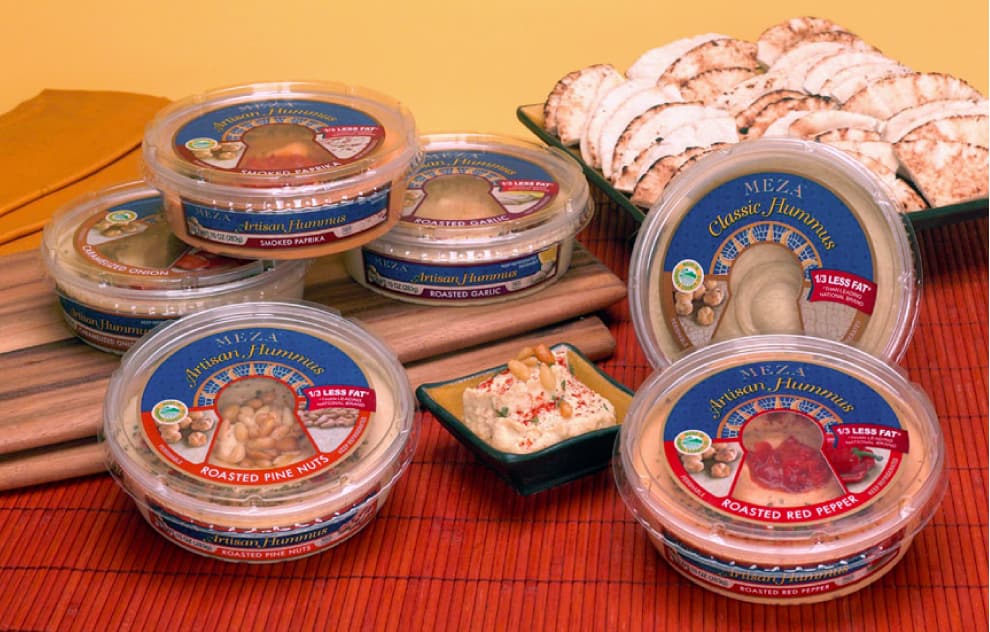 several packages of Meza Hummus and pita breadon a red tablecloth